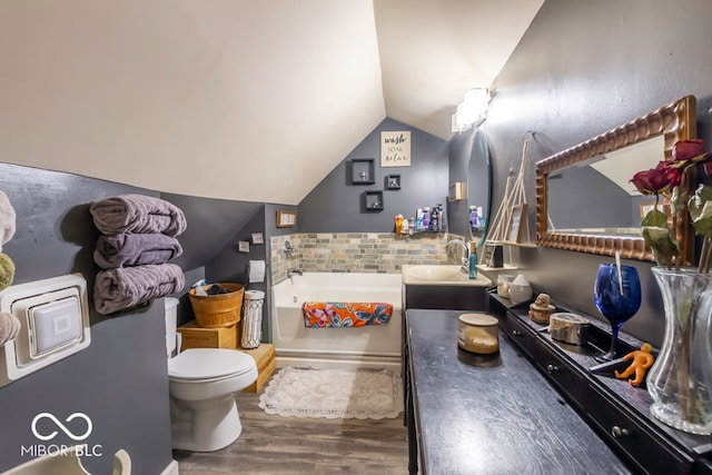 bathroom with hardwood / wood-style flooring, a washtub, lofted ceiling, vanity, and toilet