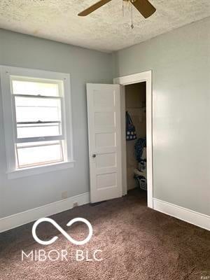 unfurnished bedroom featuring ceiling fan, a textured ceiling, and dark colored carpet