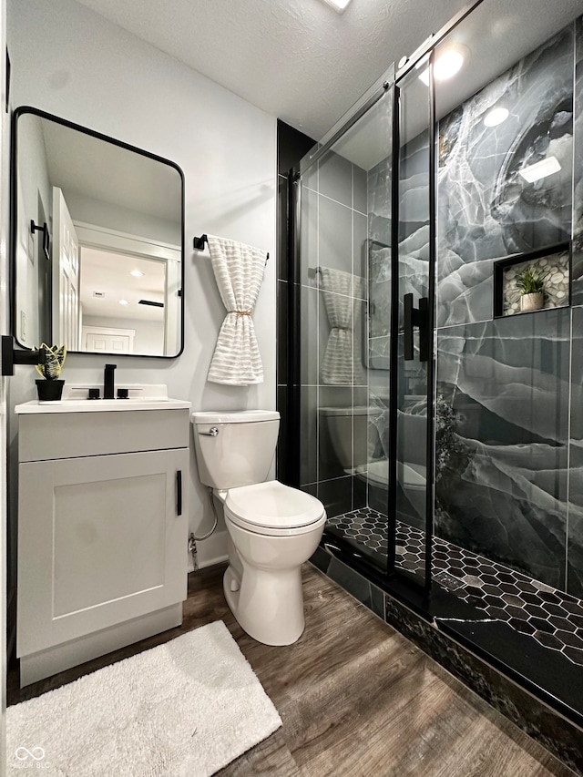 bathroom featuring toilet, a shower with door, hardwood / wood-style floors, a textured ceiling, and vanity