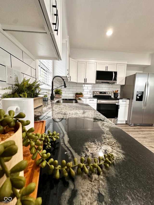 kitchen featuring stainless steel appliances, dark stone counters, light wood-type flooring, white cabinetry, and sink