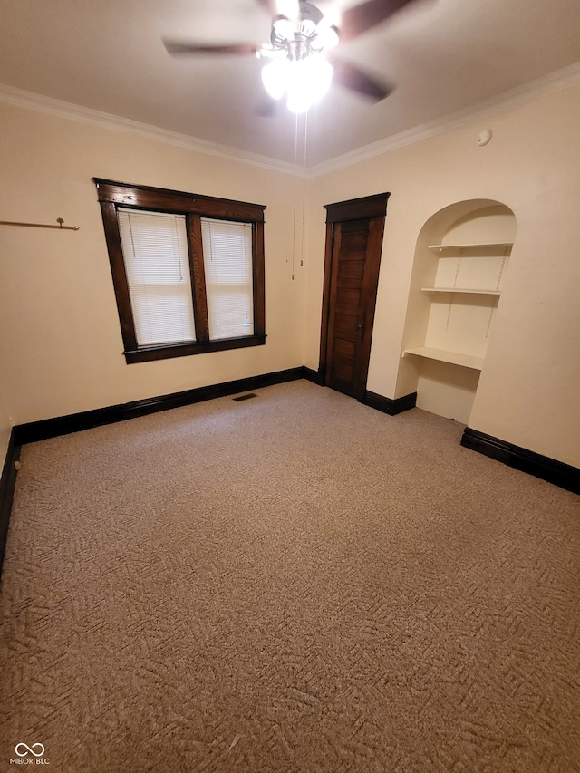 unfurnished room with built in features, ornamental molding, ceiling fan, and light colored carpet