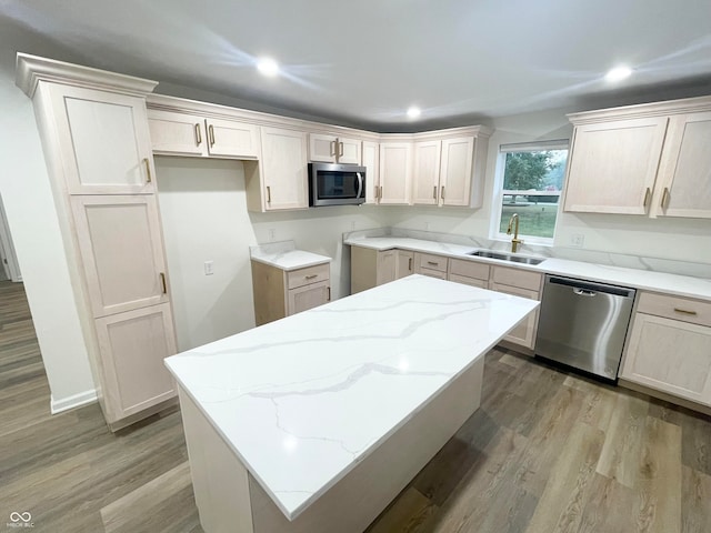 kitchen with light stone counters, light hardwood / wood-style floors, sink, a kitchen island, and appliances with stainless steel finishes