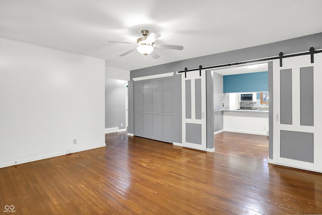 unfurnished bedroom with a barn door, ceiling fan, a closet, and hardwood / wood-style flooring