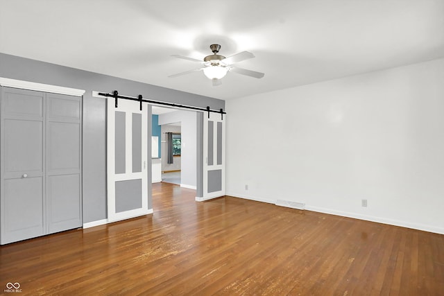 unfurnished bedroom featuring ceiling fan, hardwood / wood-style flooring, and a barn door