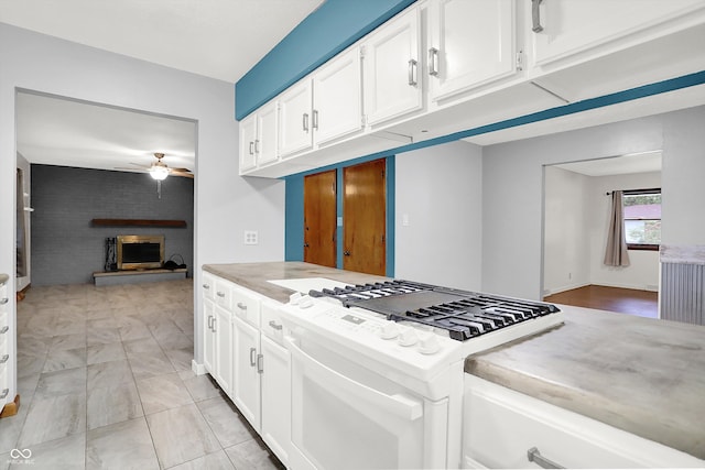 kitchen with white cabinetry, a large fireplace, ceiling fan, and white gas range oven