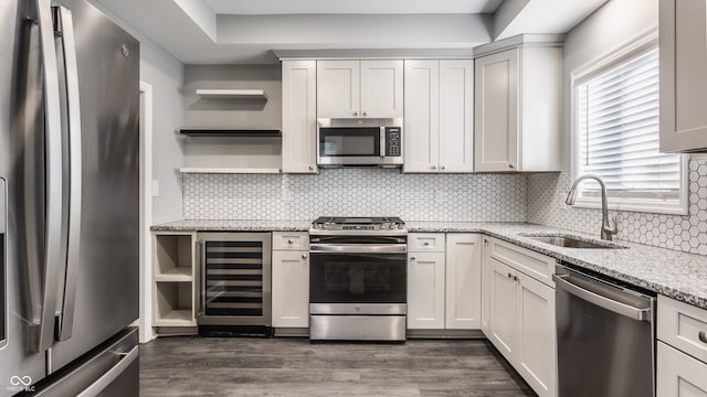 kitchen with light stone counters, dark hardwood / wood-style floors, sink, beverage cooler, and appliances with stainless steel finishes