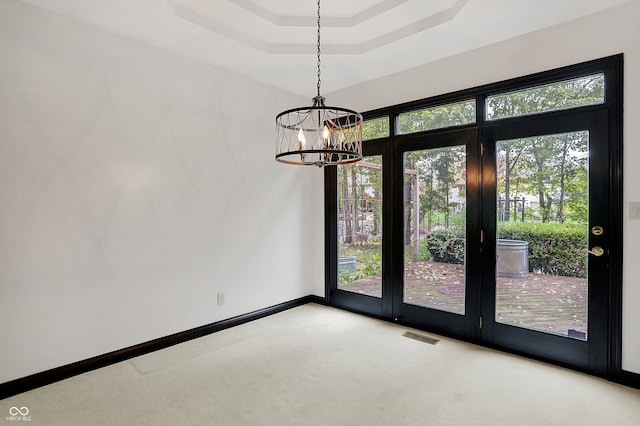 spare room featuring light carpet, an inviting chandelier, and a tray ceiling