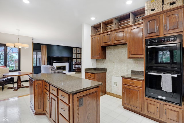 kitchen with pendant lighting, a kitchen island, backsplash, double oven, and dark stone countertops