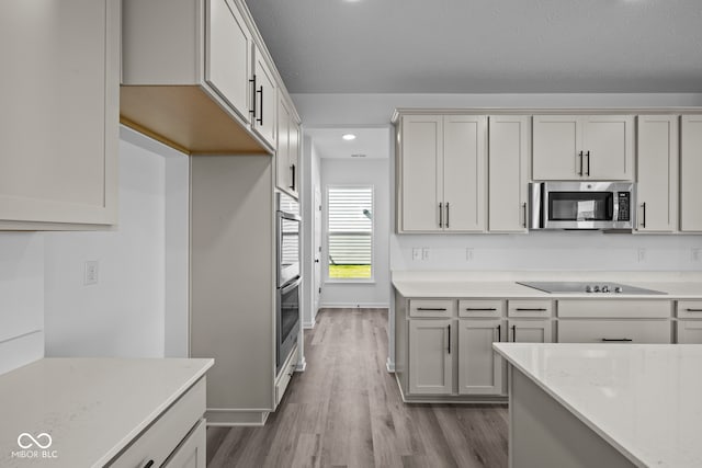 kitchen featuring stainless steel appliances, white cabinetry, light stone counters, a textured ceiling, and light hardwood / wood-style floors