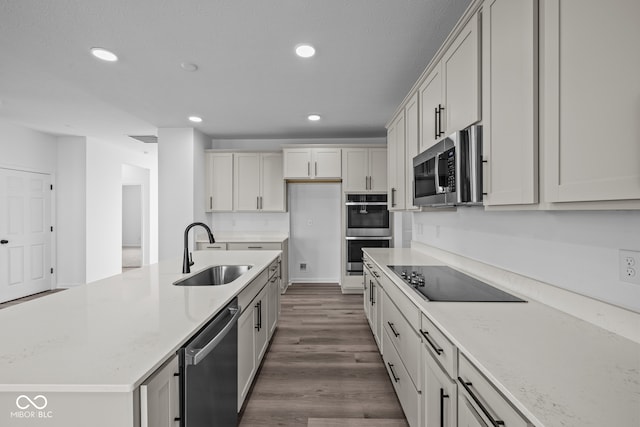 kitchen with stainless steel appliances, wood-type flooring, sink, white cabinets, and light stone counters