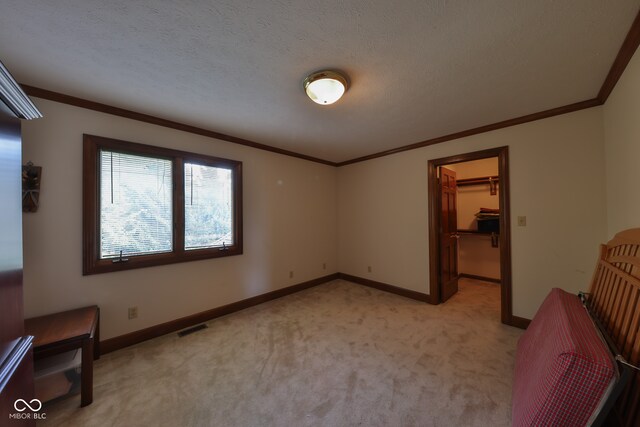 unfurnished bedroom featuring a textured ceiling, a closet, a spacious closet, light carpet, and crown molding