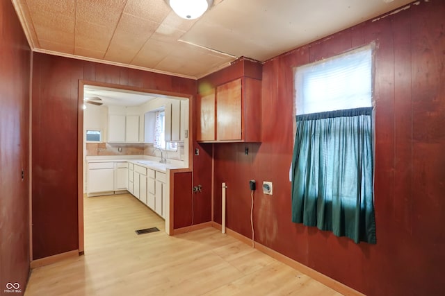 kitchen with sink, white cabinets, light hardwood / wood-style flooring, wooden walls, and ornamental molding