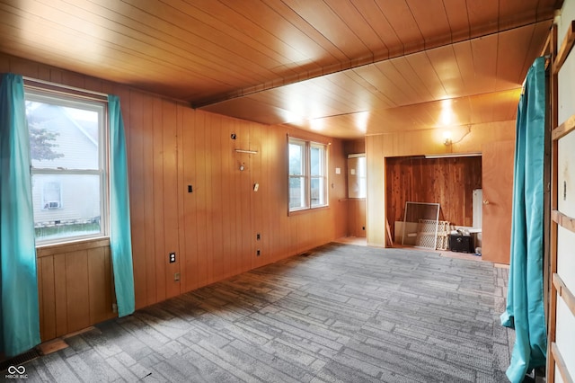 empty room featuring beamed ceiling, wooden walls, carpet, and wooden ceiling