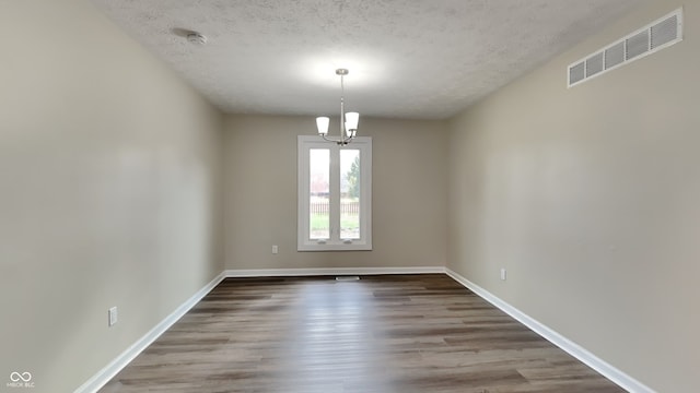 unfurnished room with a textured ceiling, wood-type flooring, and a chandelier