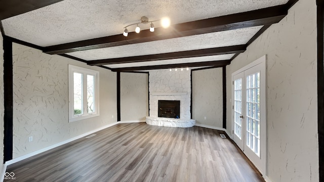 unfurnished living room with a healthy amount of sunlight, beamed ceiling, french doors, and hardwood / wood-style flooring