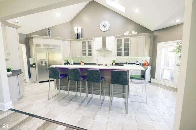 kitchen with stainless steel built in fridge, white cabinets, a kitchen breakfast bar, high vaulted ceiling, and wall chimney exhaust hood