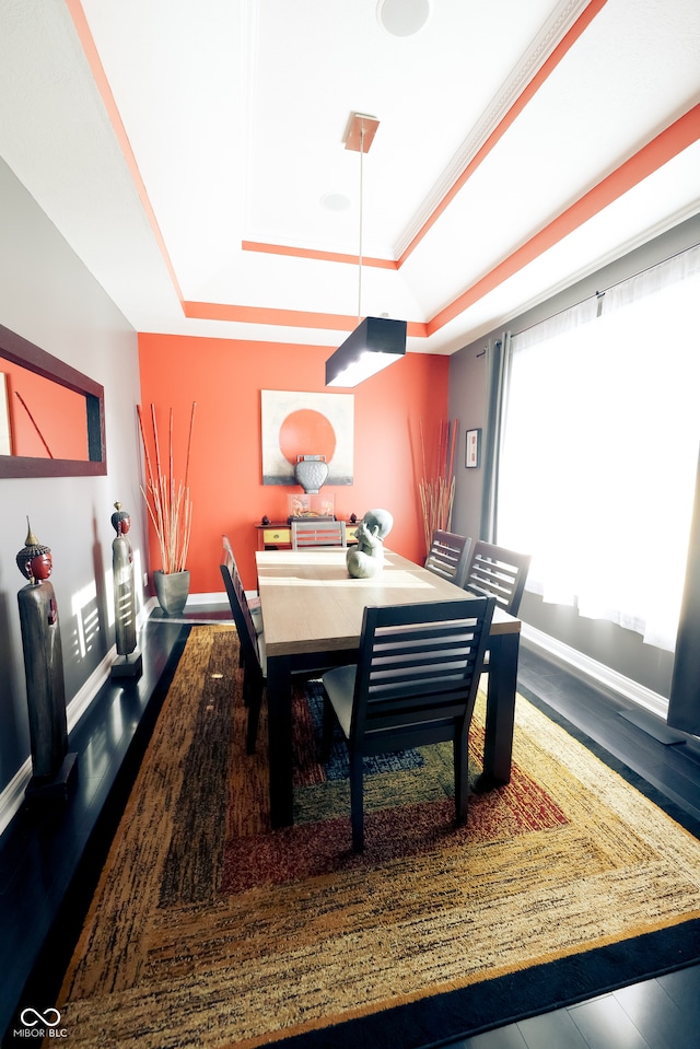 dining space with ornamental molding, wood-type flooring, and a tray ceiling