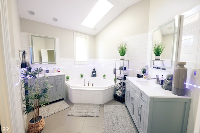 bathroom with tile patterned floors, tiled bath, tile walls, vanity, and lofted ceiling with skylight