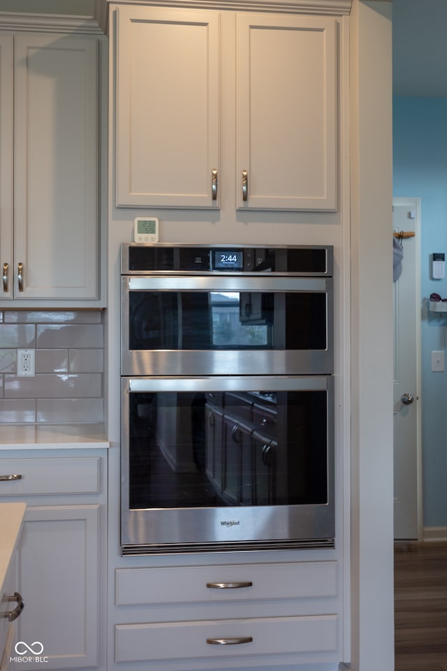 kitchen featuring stainless steel double oven, backsplash, white cabinetry, and hardwood / wood-style floors