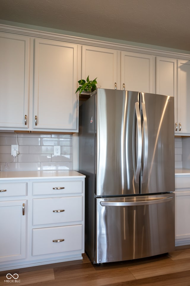 kitchen with white cabinets, stainless steel refrigerator, hardwood / wood-style floors, and decorative backsplash