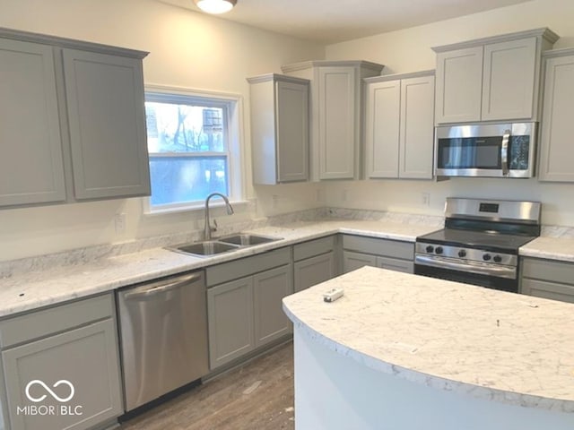 kitchen with gray cabinetry, sink, dark wood-type flooring, light stone counters, and appliances with stainless steel finishes