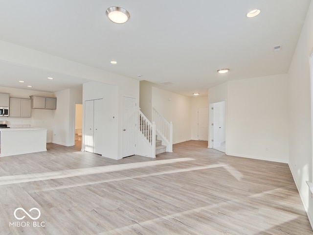 unfurnished living room with light wood-style floors, recessed lighting, baseboards, and stairs