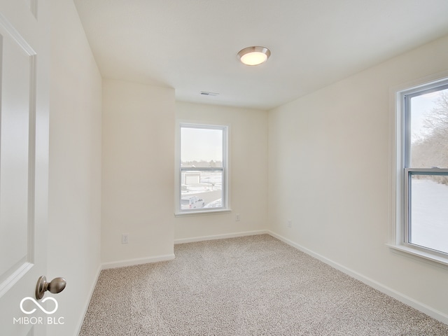 carpeted spare room with a healthy amount of sunlight, baseboards, and visible vents