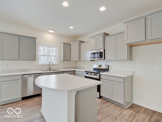 kitchen featuring light wood-style flooring, a center island, stainless steel appliances, light countertops, and a sink