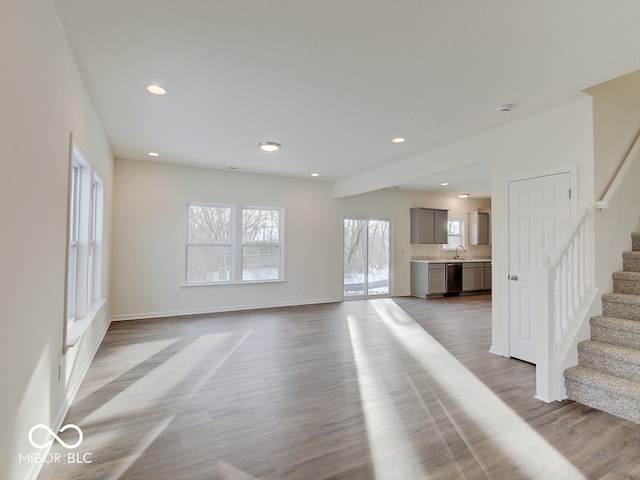 unfurnished living room featuring baseboards, light wood-style flooring, stairs, a sink, and recessed lighting