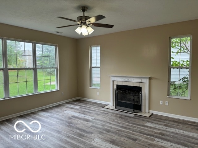 unfurnished living room featuring ceiling fan, a tiled fireplace, hardwood / wood-style floors, and a wealth of natural light