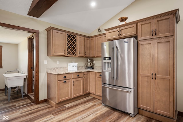 kitchen featuring wood-type flooring, light stone countertops, lofted ceiling, and stainless steel fridge with ice dispenser