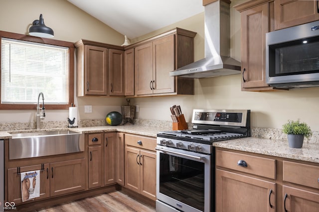 kitchen with lofted ceiling, sink, wall chimney range hood, stainless steel appliances, and light hardwood / wood-style floors