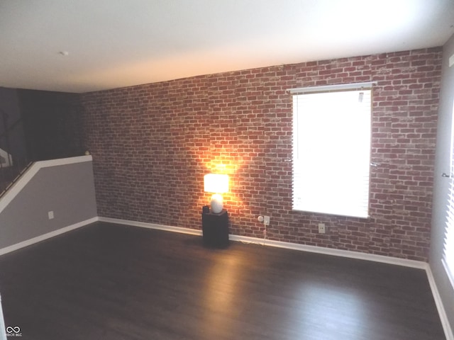 spare room with brick wall, dark hardwood / wood-style flooring, and a wealth of natural light