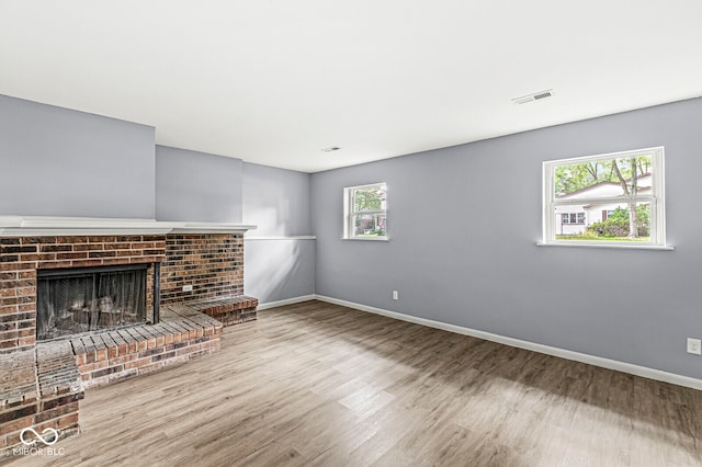 unfurnished living room featuring a brick fireplace, a wealth of natural light, and wood-type flooring