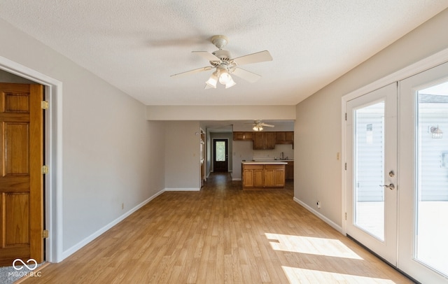 unfurnished living room featuring light hardwood / wood-style floors, ceiling fan, sink, and a textured ceiling