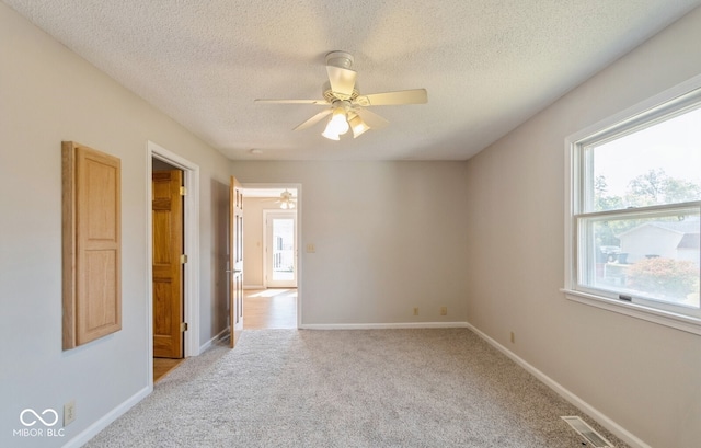 spare room featuring a textured ceiling, ceiling fan, light colored carpet, and a wealth of natural light