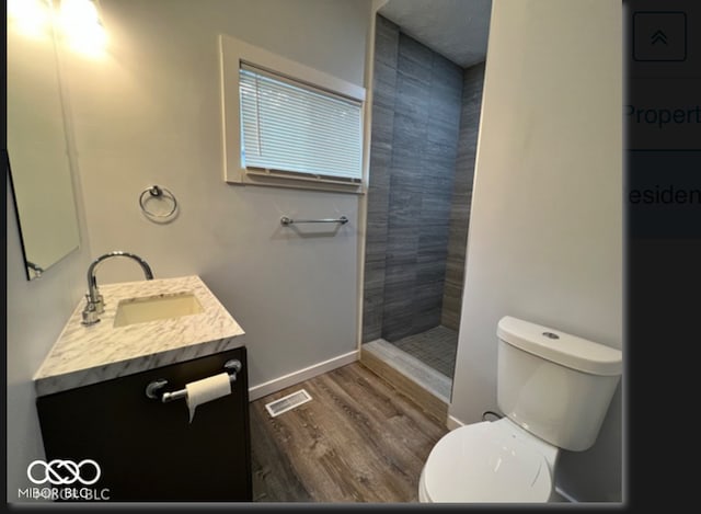 bathroom featuring tiled shower, hardwood / wood-style flooring, vanity, and toilet