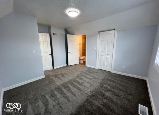 unfurnished bedroom featuring dark colored carpet, lofted ceiling, ensuite bath, and a closet