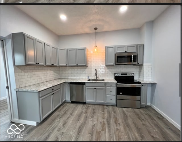 kitchen featuring tasteful backsplash, gray cabinetry, wood-type flooring, decorative light fixtures, and stainless steel appliances