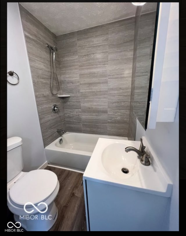 full bathroom with vanity, a textured ceiling, tiled shower / bath combo, wood-type flooring, and toilet