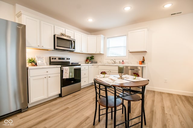 kitchen with light hardwood / wood-style flooring, white cabinets, and stainless steel appliances