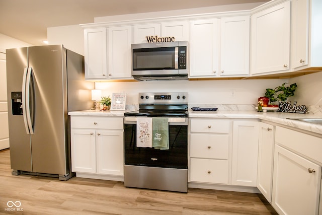 kitchen with white cabinets, appliances with stainless steel finishes, light wood-type flooring, and light stone countertops