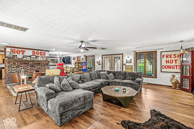 living room featuring a textured ceiling, wood-type flooring, ceiling fan, and a brick fireplace