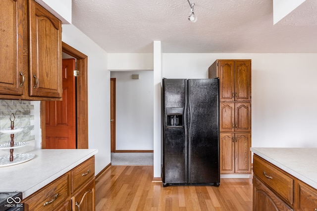 kitchen featuring black fridge with ice dispenser, light hardwood / wood-style flooring, and a textured ceiling