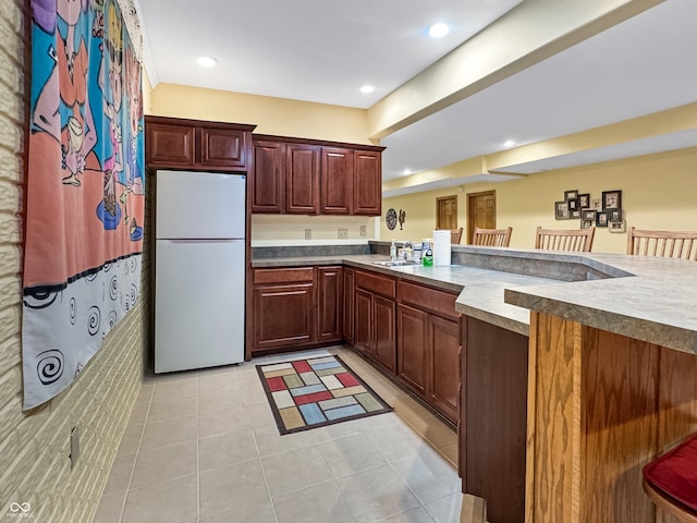 kitchen featuring sink, light tile patterned floors, white refrigerator, and kitchen peninsula