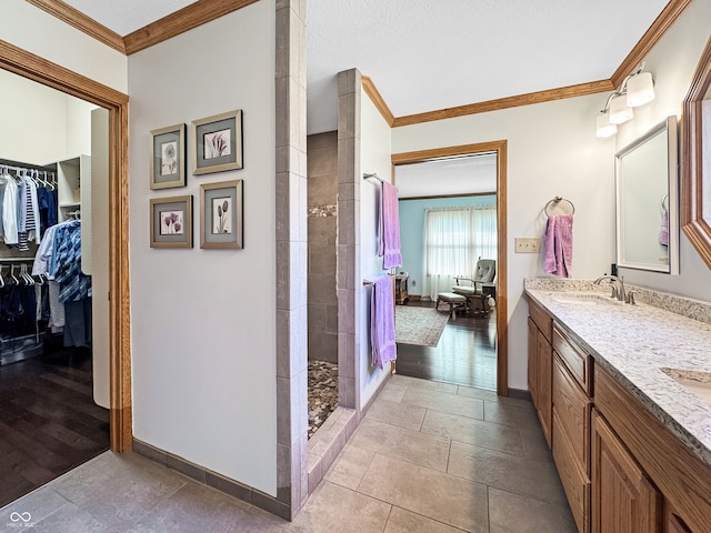 bathroom with a tile shower, vanity, crown molding, and tile patterned flooring