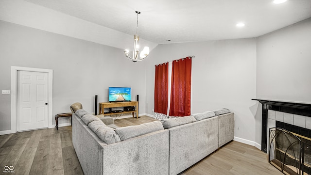 living room with lofted ceiling, a notable chandelier, a tiled fireplace, and light hardwood / wood-style floors