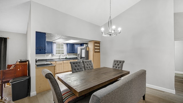 dining space with high vaulted ceiling, sink, light wood-type flooring, and an inviting chandelier