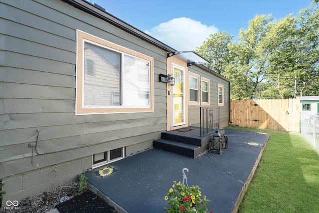 view of exterior entry featuring a patio and a lawn