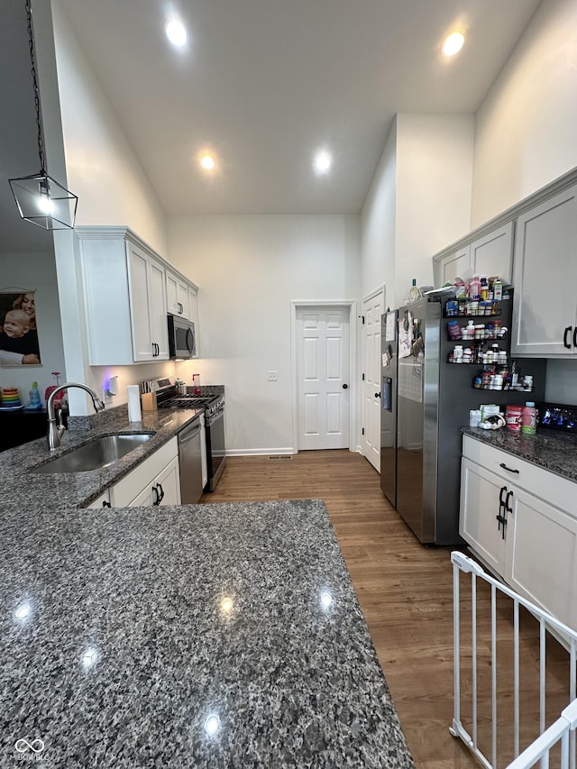kitchen featuring dark stone counters, a high ceiling, appliances with stainless steel finishes, and a sink